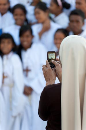 A nun photographs choir members after Sunday mass. When we left the church, the second mass was about to commence and the choir members quickly huddled outdoors for a photo opportunity as this nun, their choir director snapped them with her mobile phone