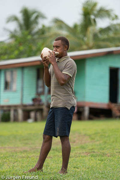 Fijian man blows a conch shell to summon the adults in the community for a meeting.