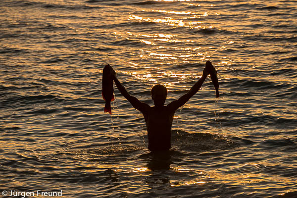 Man holding up freshly caught reef fish silhouetted against the sunset from Ligau Village coast.