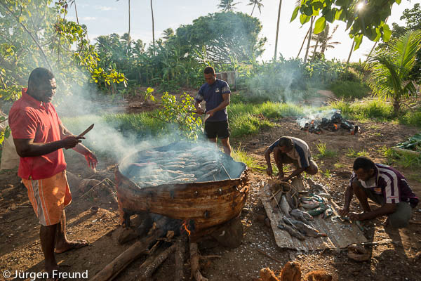 Yadua Village men prepare and cook on an open fire the freshly caught fish for a funeral community feast.